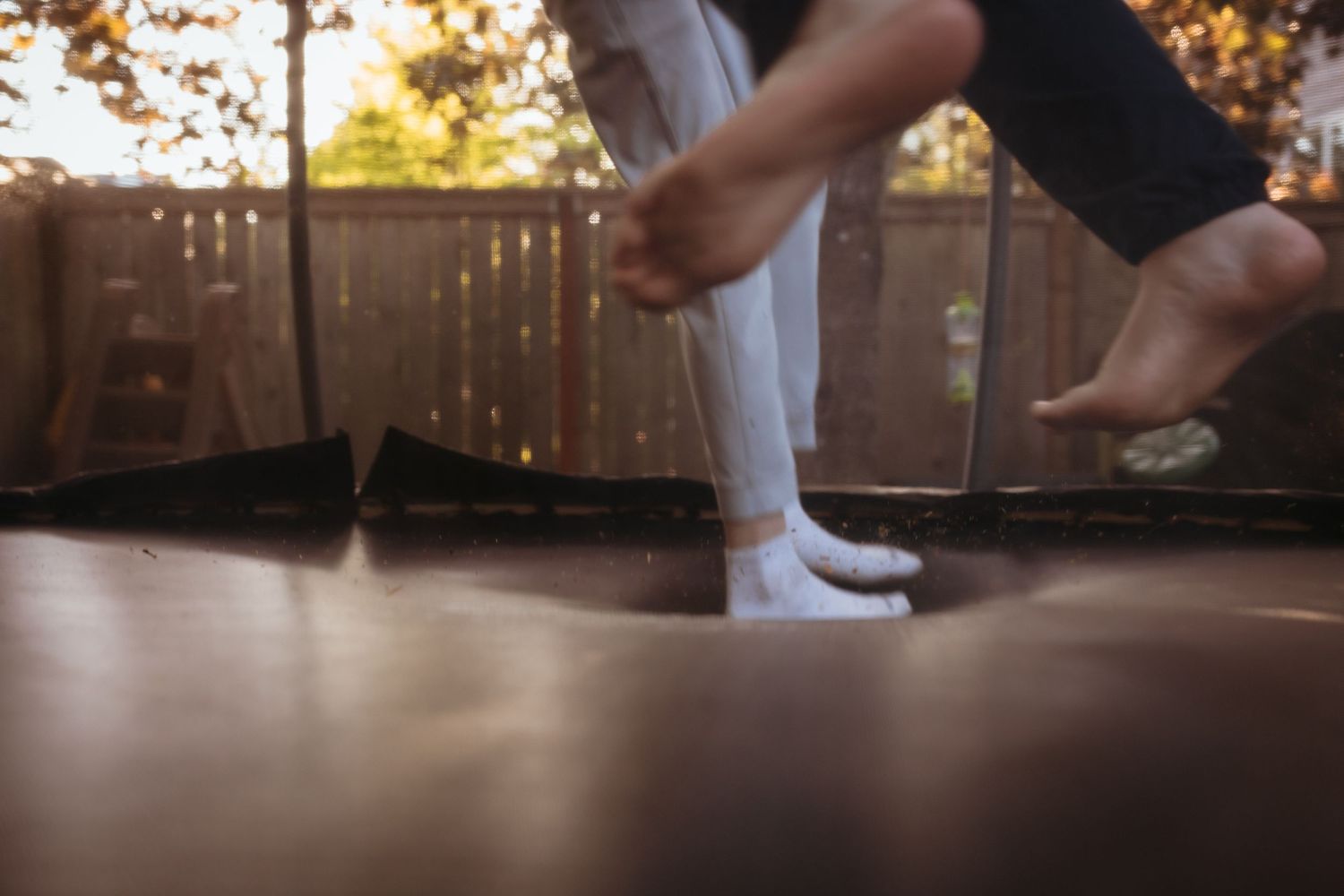 Person jumping on a backyard trampoline wearing white socks on a sunny autumn day.