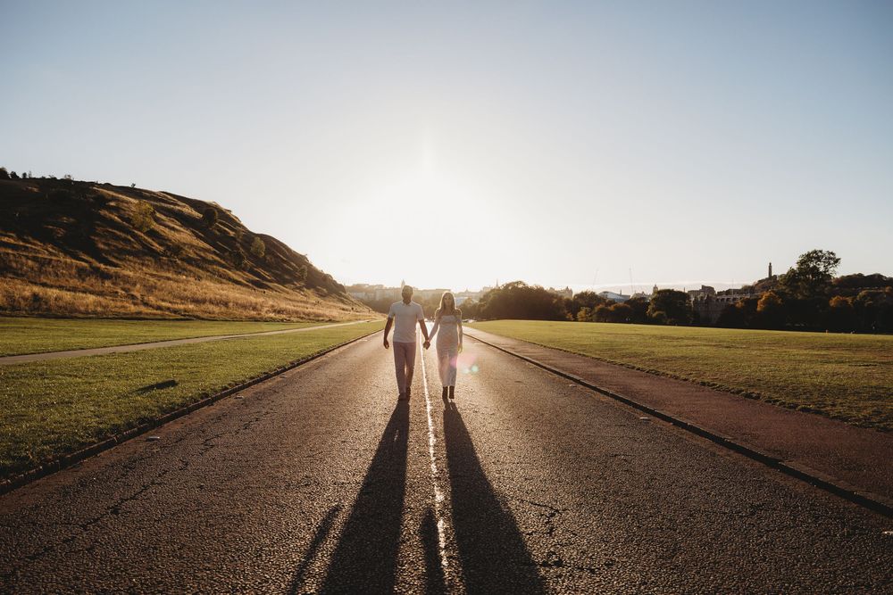 Two people walking together on an empty country road at sunset creating a silhouette against the golden sky.