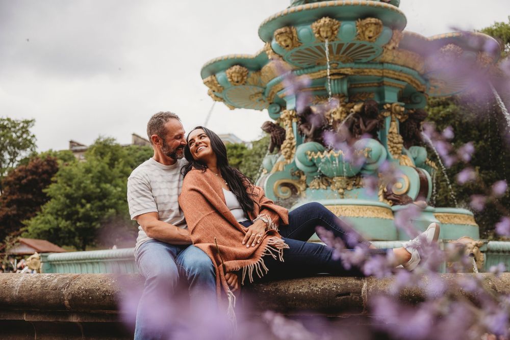 A romantic couple embraces in a garden setting with soft purple flowers in the foreground during golden hour.