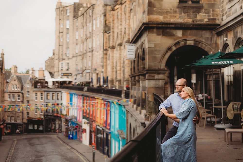 A couple dances together on a historic cobblestone street lined with classic European architecture and storefronts.