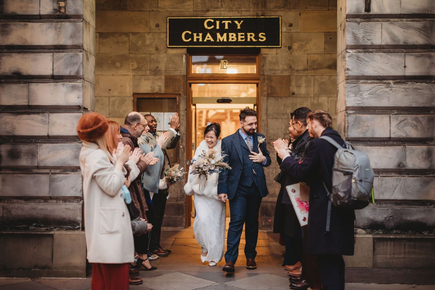 Newlyweds exit City Chambers Edinburgh surrounded by cheering guests after their wedding ceremony.