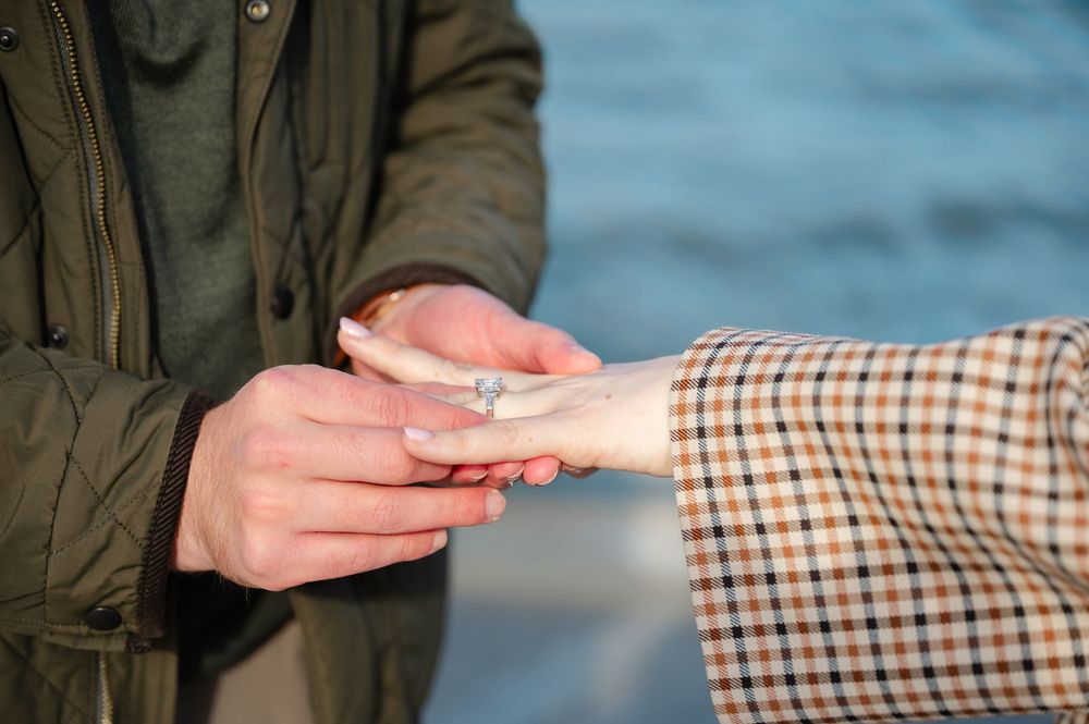 Close-up of a romantic marriage proposal with a diamond engagement ring being placed on a woman's finger outdoors.