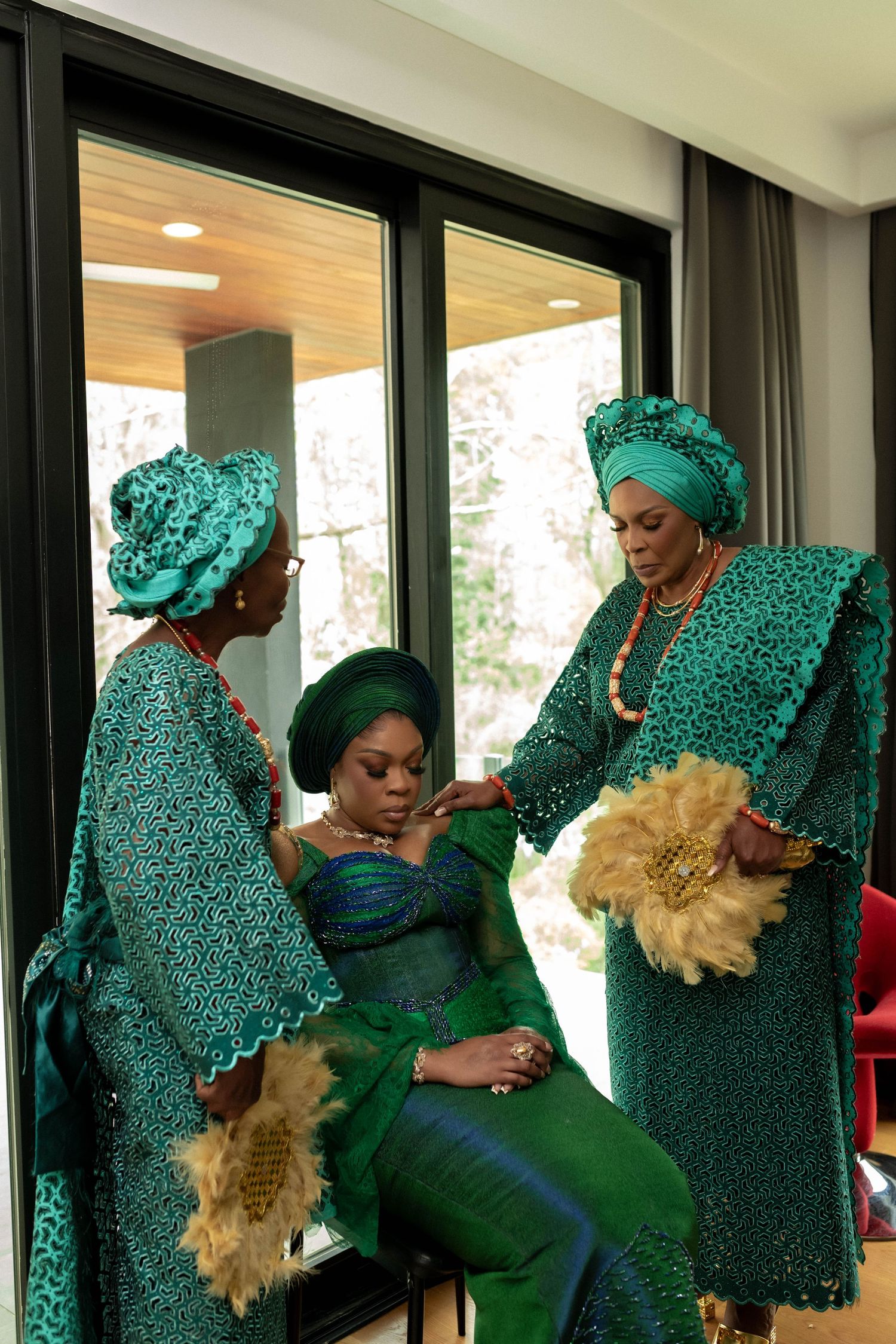 Three women in elegant green traditional Nigerian attire and gele headwraps prepare for a ceremonial celebration.