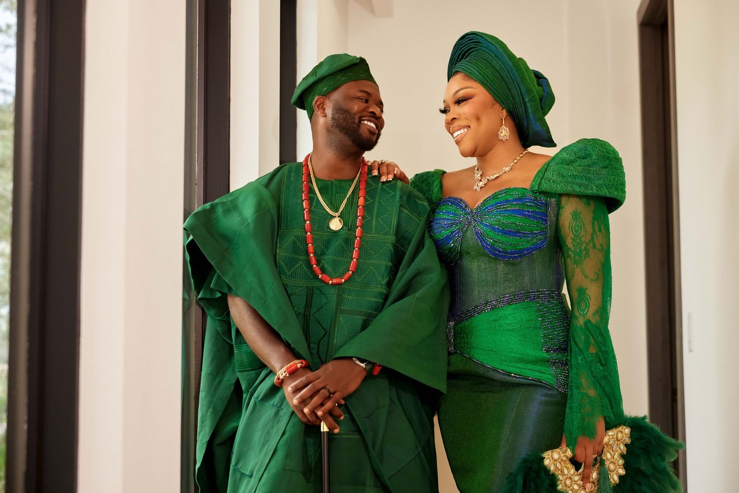 Couple in matching green traditional Nigerian attire smiling together, wearing gele headwrap and agbada with gold beads.