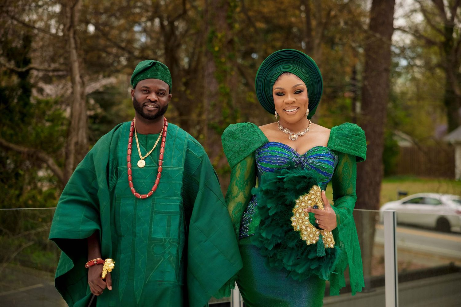 Couple in matching emerald green Nigerian traditional attire, man in agbada and woman in gele headwrap, posing outdoors.