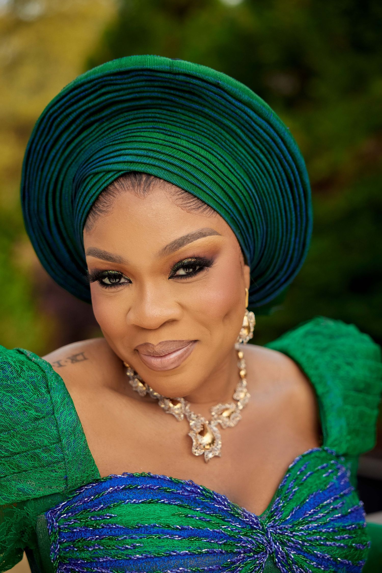 Woman in elegant green lace dress and matching gele headwrap with gold jewelry at a formal event.