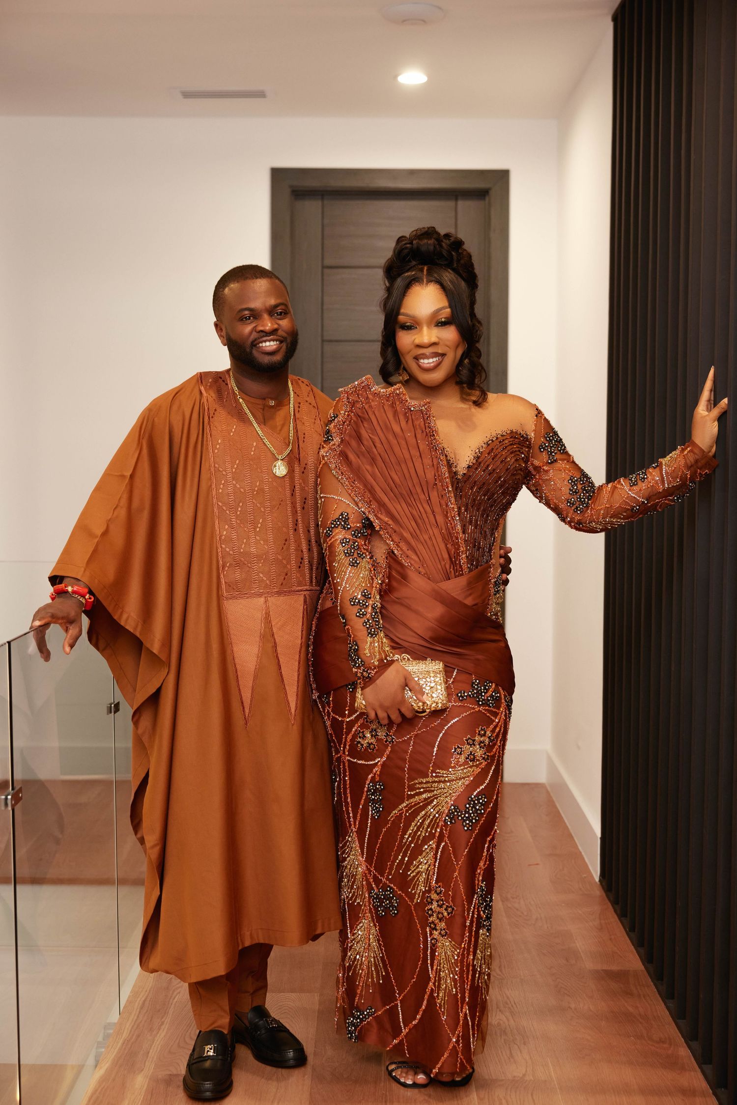 Couple wearing matching rust brown African traditional attire, posing elegantly indoors for a formal occasion.