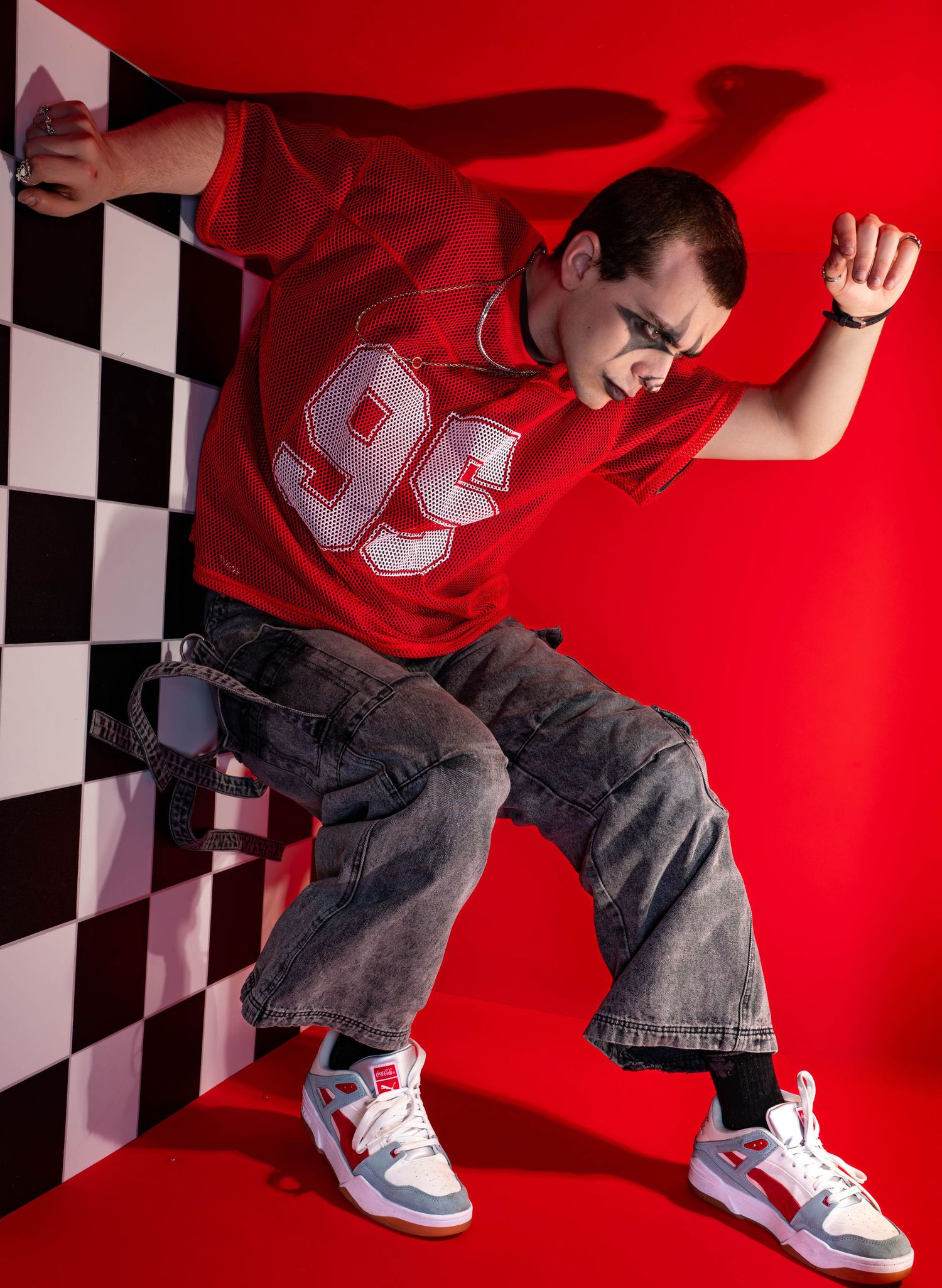 Young man in red jersey #99, baggy jeans, and sneakers striking a dynamic dance pose against a red backdrop.