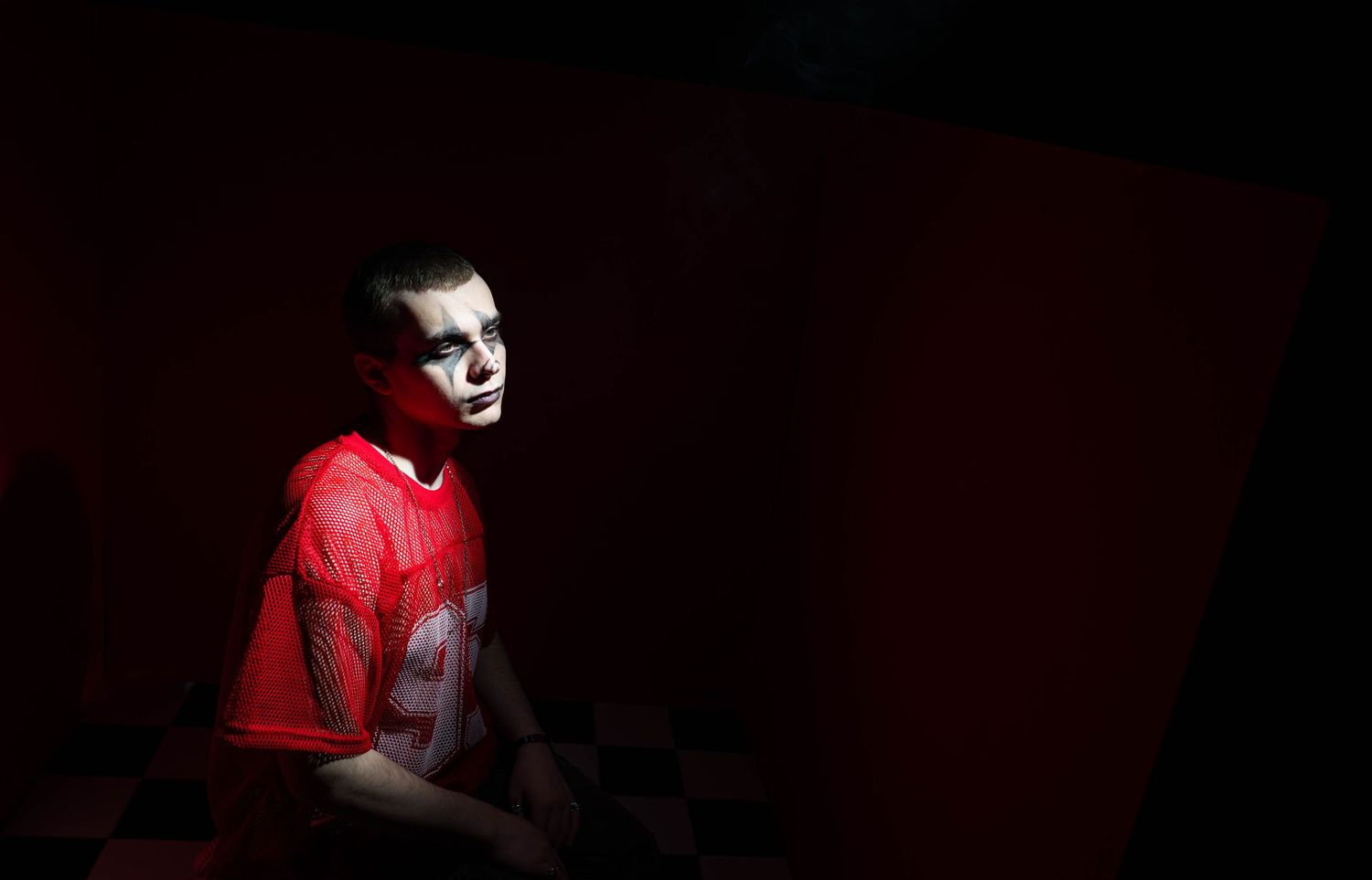 Boy in red jersey with face paint sits in dramatic lighting against a dark background.