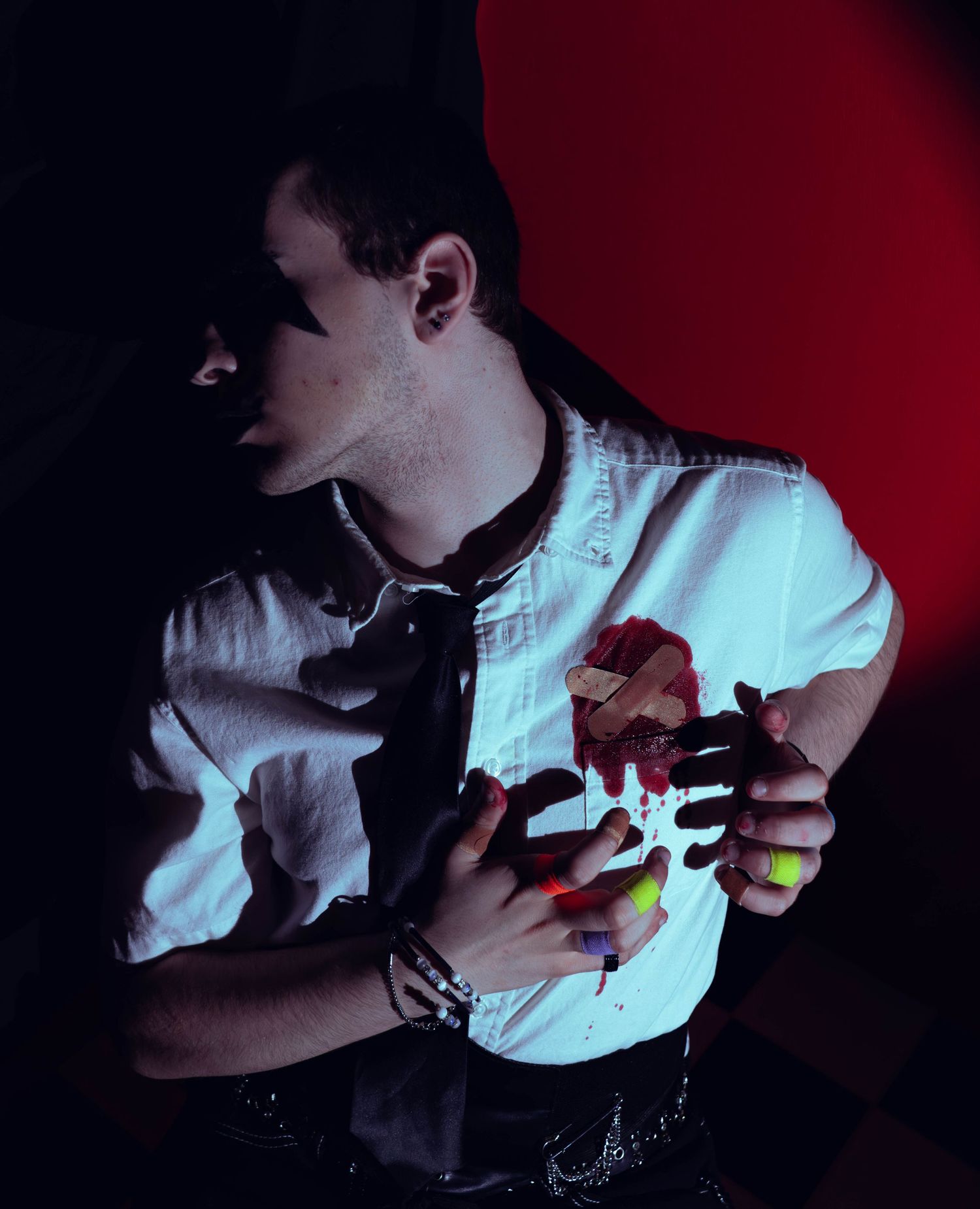 Young man in white shirt holding colorful painted hands against chest in dramatic red and dark artistic photography.