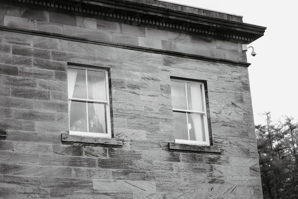 Black and white photo of a historic sandstone building corner with two large sash windows and ornate cornice detailing.