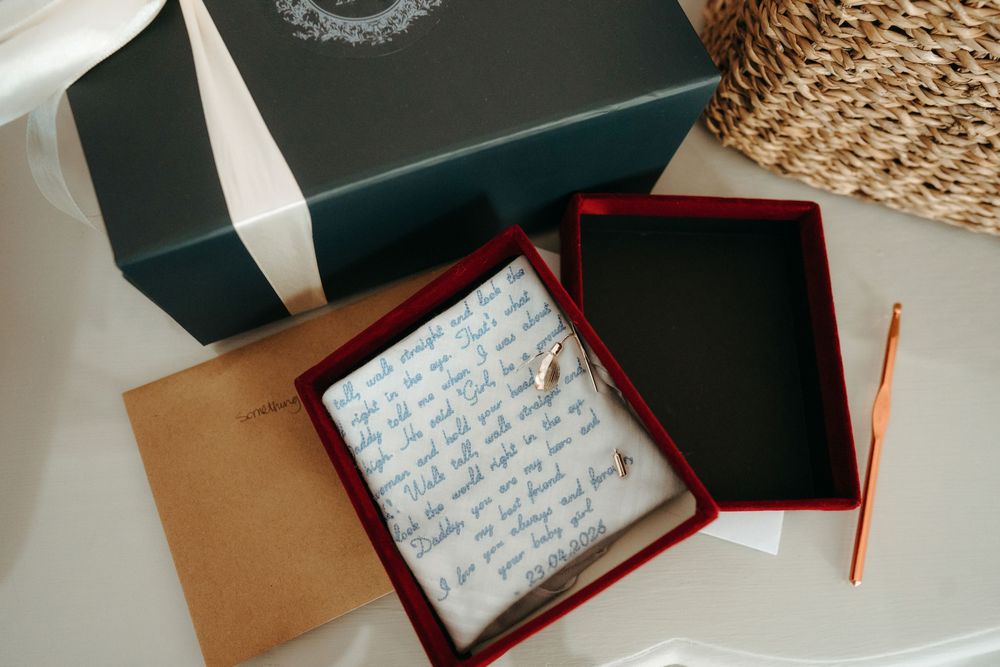 Open dark green gift box with red interior, tissue paper, small gold charm, kraft envelope, and pencil on white surface.