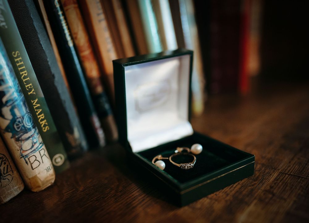 Pearl and gold rings displayed in a green velvet jewelry box on a wooden table with vintage books in the background.