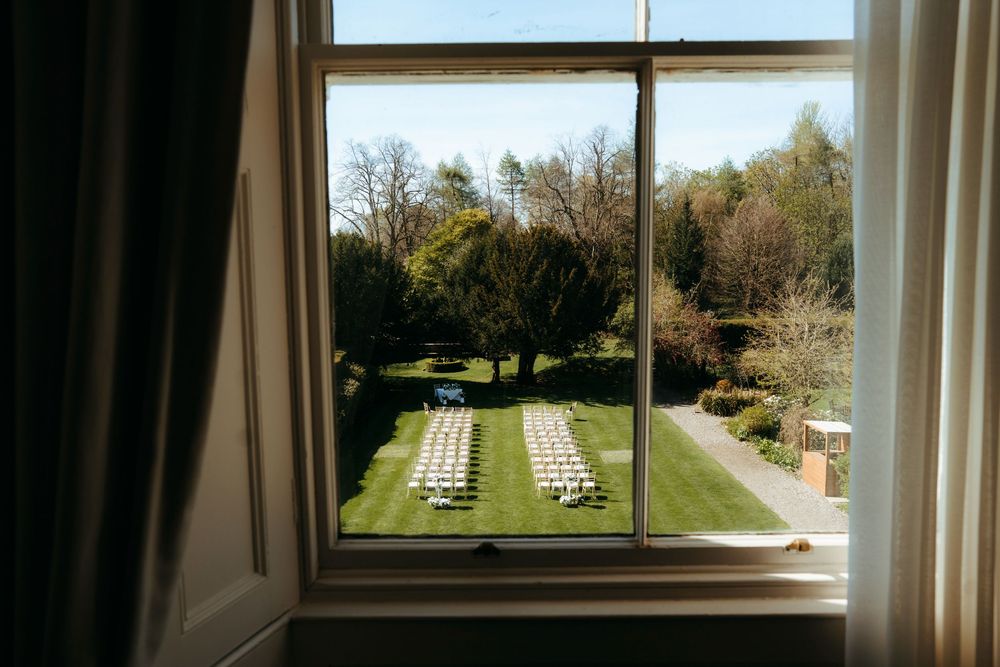 View through a window of an outdoor wedding ceremony setup with white chairs on a lush green lawn.