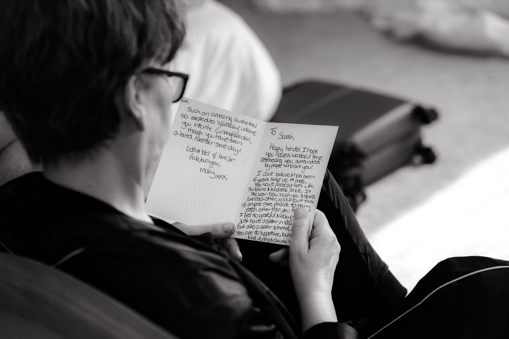Black and white photo of a person wearing glasses reading a handwritten letter while seated indoors.