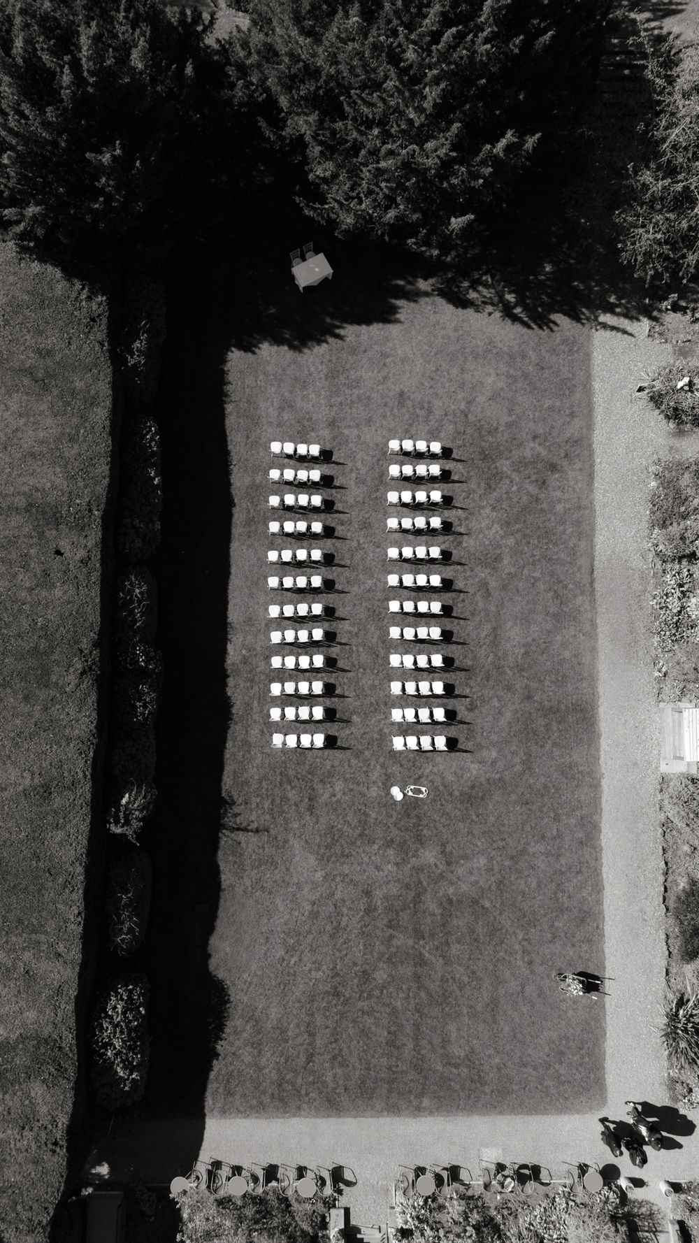 Aerial black and white drone photo of rows of white chairs arranged for an outdoor ceremony on a grass lawn.