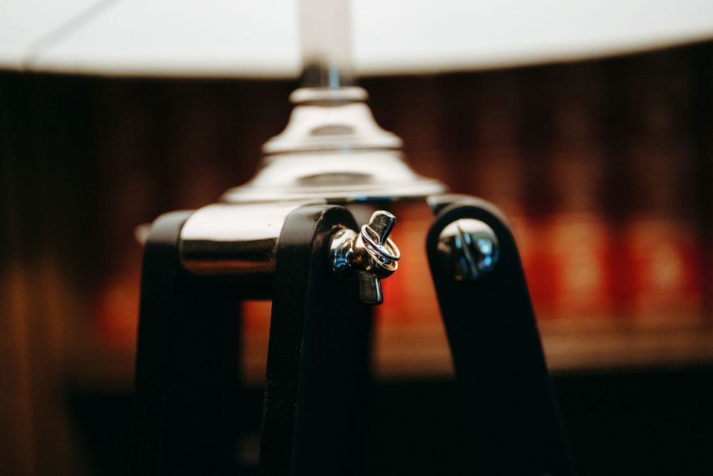 Close-up of wedding rings resting on a black lamp base with a blurred bokeh background.