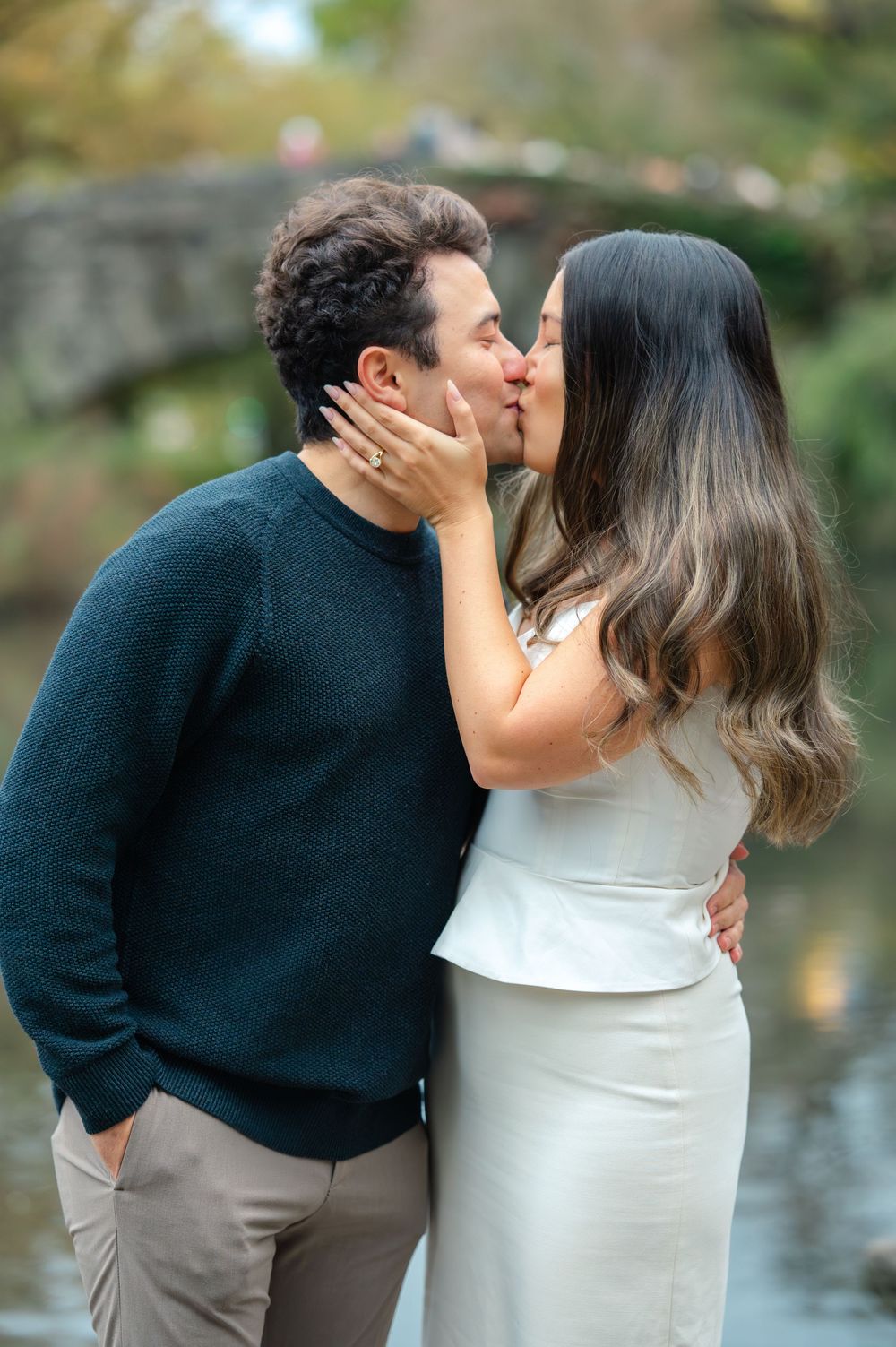 Couple sharing a romantic kiss near a bridge and pond in Central Park during their engagement session.