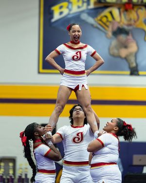 Cheerleader in white and red uniform balances atop teammates in stunt.