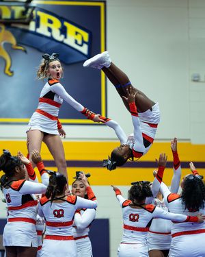 Cheerleaders in orange and white perform aerial stunt at competition.