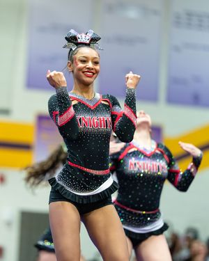 Smiling Knights cheerleader in black uniform performs energetic routine at indoor cheer competition.