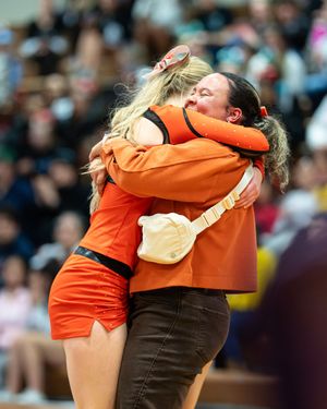 Two cheerleaders in orange uniforms share an emotional hug during a cheerleading competition event.
