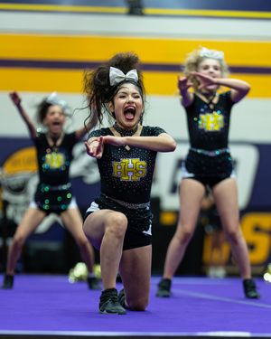 Cheerleader in black uniform performs an energetic routine with teammates during a competitive cheer event.