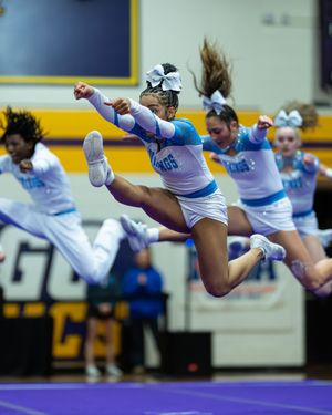 A cheerleader in a blue and white uniform leaps high in the air during a cheerleading competition.
