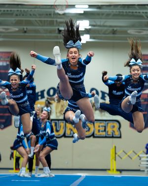 Lancers cheerleaders in blue uniforms perform synchronized jumps at indoor cheer competition.