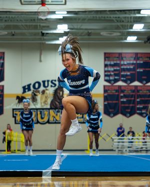 Lancers cheerleader executes high jump during performance at Hous gymnasium competition.