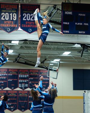 Cheerleader performs a high-flying stunt at a state championship competition in a school gymnasium.