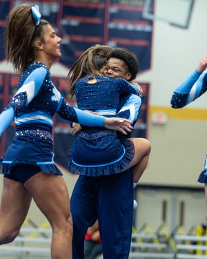 Cheerleaders in blue sparkle uniforms perform a lift stunt during a cheerleading competition.