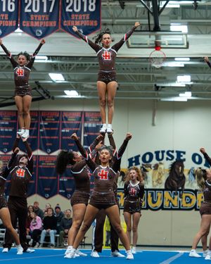 Competitive cheerleading squad performs pyramid stunt near state championship banners.