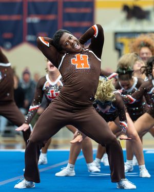 Cheerleader in brown JH uniform performs expressive dance routine.