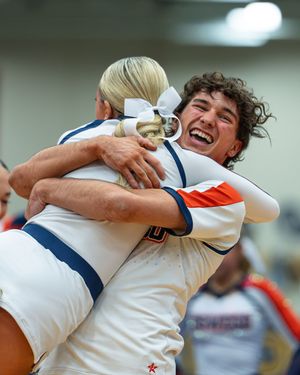 Two cheerleaders in white and orange uniforms embrace joyfully after a competition performance.