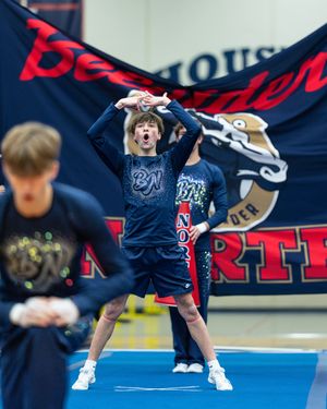 Male cheerleader in navy Bearden uniform performs energetically at indoor cheerleading competition.
