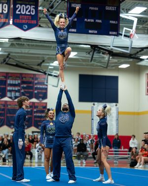 Cheerleader balances in a one-arm liberty stunt held by teammates during a competitive cheerleading performance.