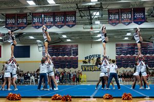 Competitive cheerleading team executes pyramid formation with pom-poms on blue mat.