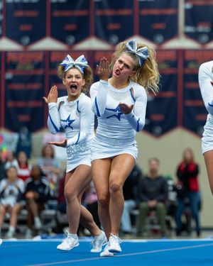 Energetic cheerleaders in white and blue star uniforms perform a routine during a competitive cheer event.