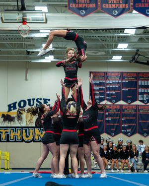 Cheerleading team performs a high-flying stunt with a flyer suspended in the air during a competition.