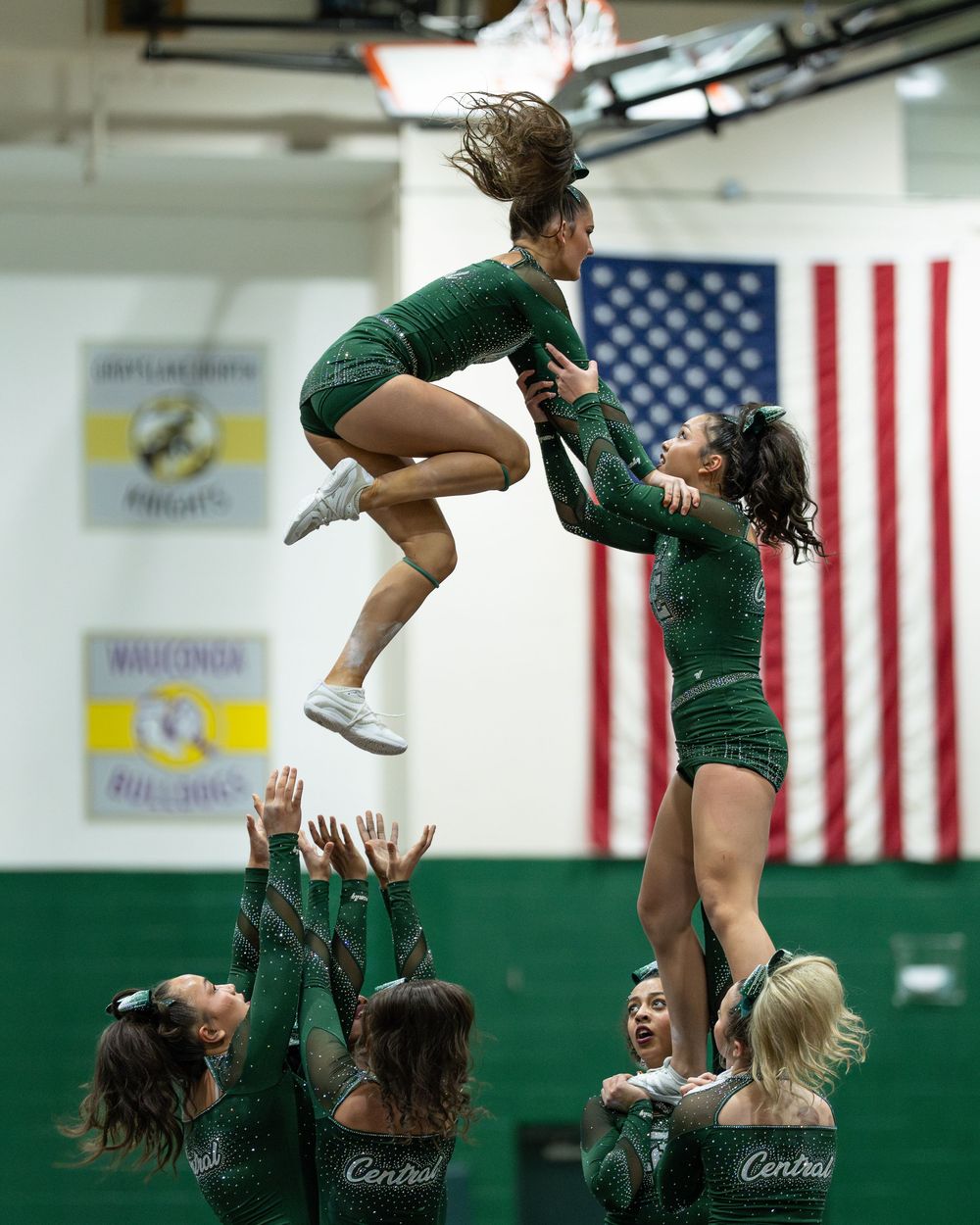 Green uniformed cheerleaders perform a high-flying stunt in a school gymnasium.