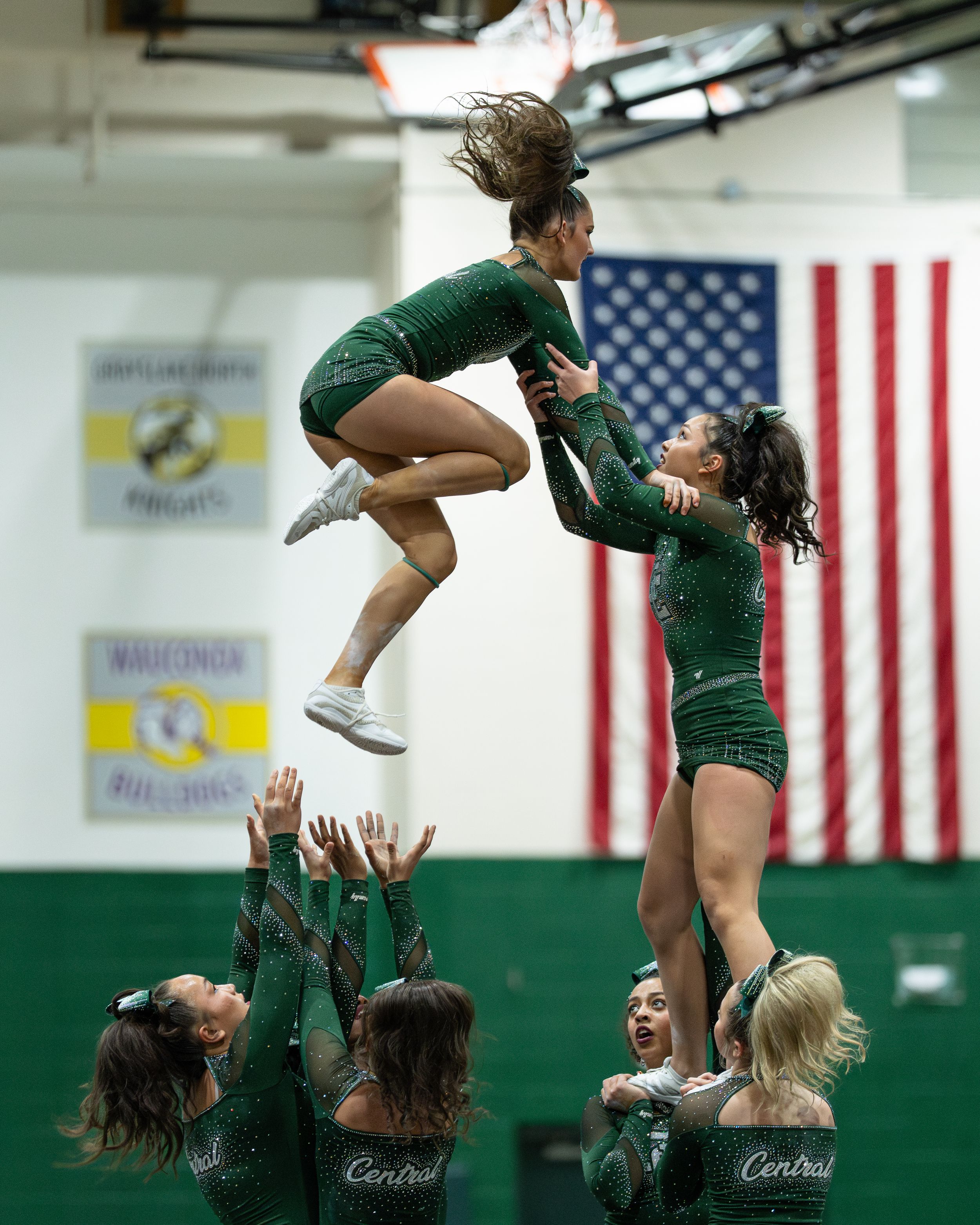 Green uniformed cheerleaders perform a high-flying stunt in a school gymnasium.