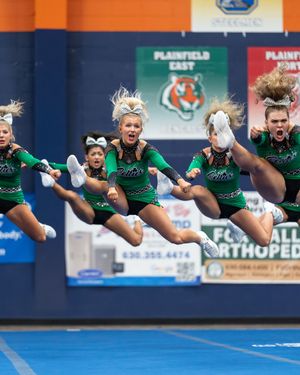 Green-uniformed cheerleaders perform synchronized toe-touch jumps at Plainfield East competition.