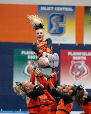 A cheerleader is tossed high in the air during a Joliet Central competition while teammates in orange uniforms provide support below.