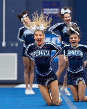 An energetic cheerleader in a navy South uniform slides on her knees with hair flying during an exciting cheerleading performance.