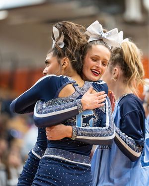 Two cheerleaders in navy rhinestone uniforms share a warm embrace after their cheerleading competition performance.