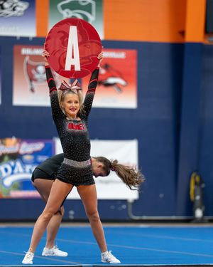 Cheerleader holds red letter A sign overhead during competitive performance.