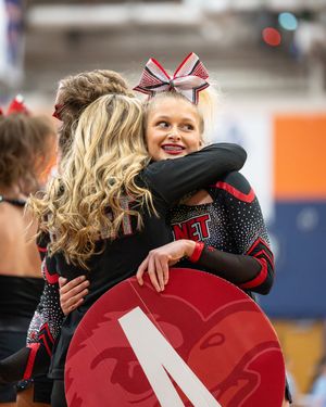 Cheerleader in black uniform hugs coach after performance at cheer competition.