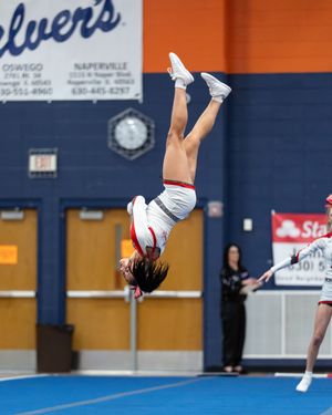 A cheerleader performs a dramatic back flip during a competitive cheerleading event in a school gymnasium.