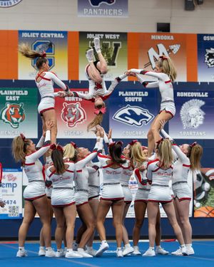 A cheerleading squad in white and red uniforms executes a complex multi-level stunt pyramid at competition.
